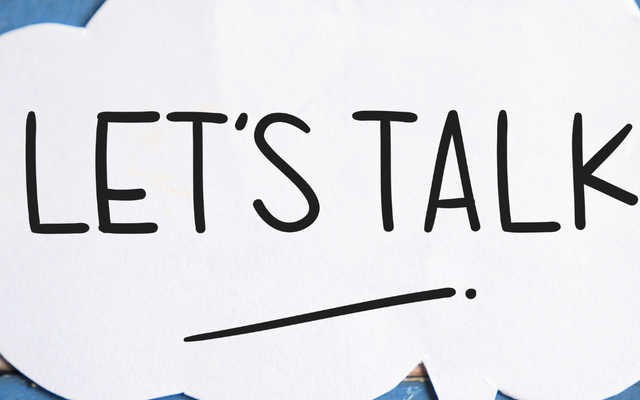 Ein weißes Sprechblasen-Ausschnitt mit der Aufschrift „LET’S TALK“ (Lass uns reden) liegt auf einem blauen, strukturierten Holzhintergrund.